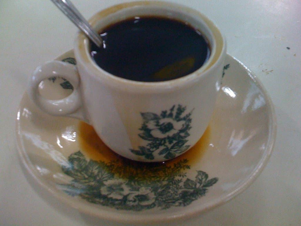 A traditional cup of kopi-o, black coffee sweetened with sugar, served in a ceramic cup and saucer.